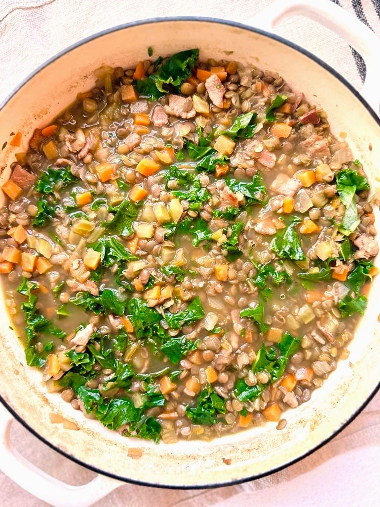 Dutch oven filled with cooked bacon lentil soup with added shredded kale leaves.