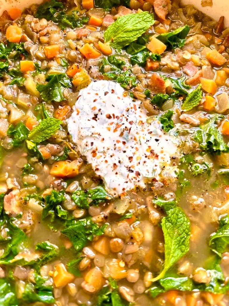 Close up image of bacon lentil soup, topped with Greek yogurt and garnished with fresh mint leaves.
