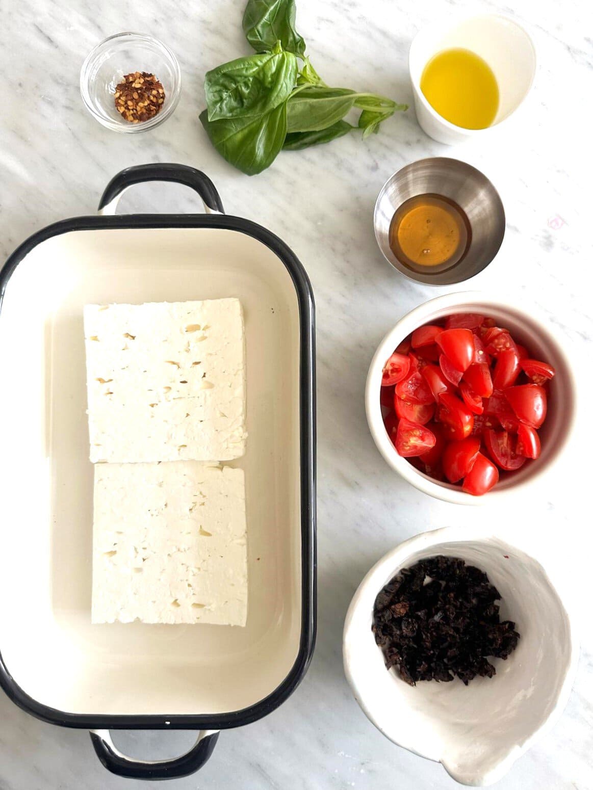 Individual recipe ingredients for hot baked feta cheese dip, set out on a worktop.