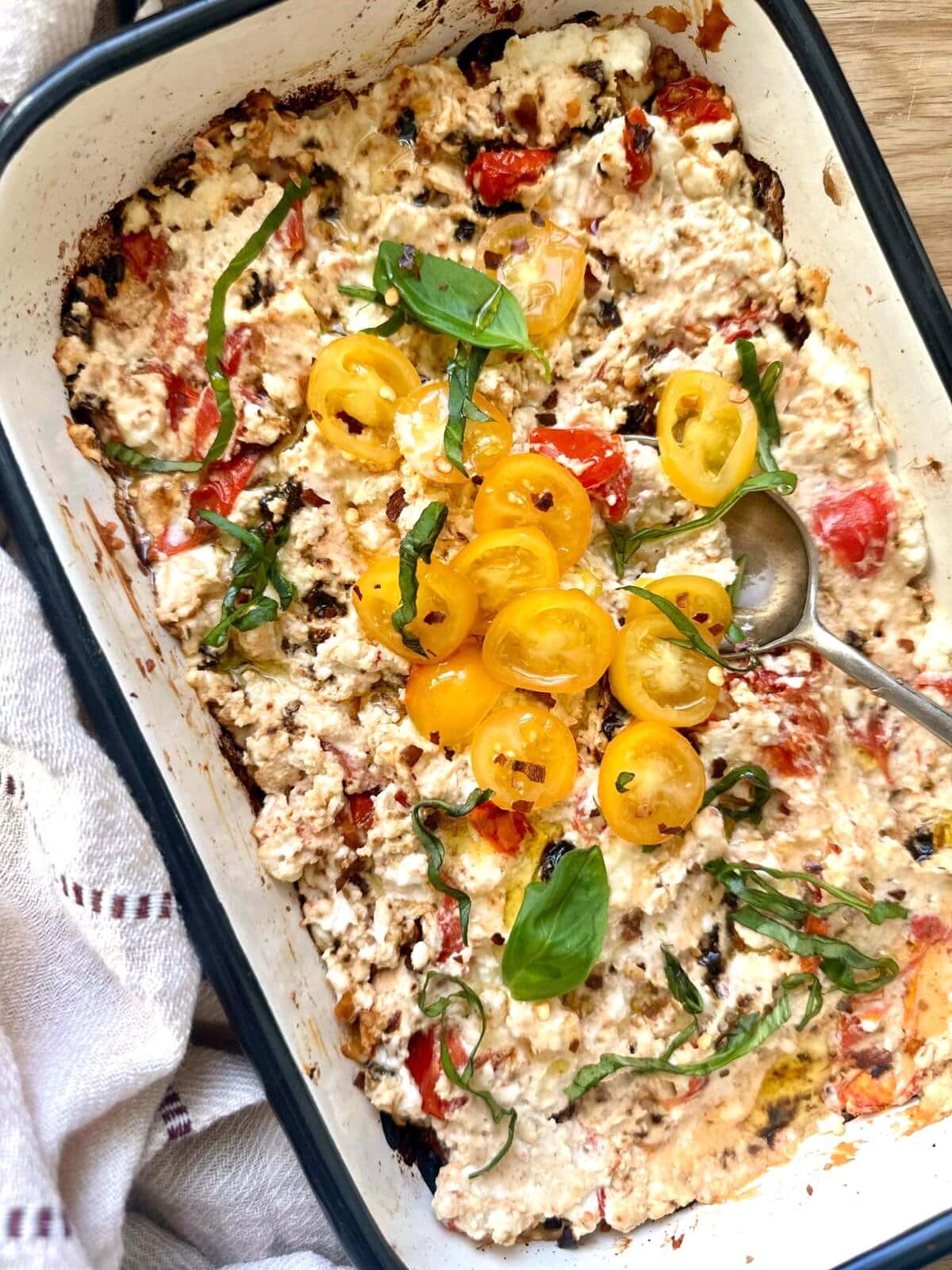 A shallow dish of hot baked feta cheese dip, topped with fresh tomatoes and shredded basil leaves.