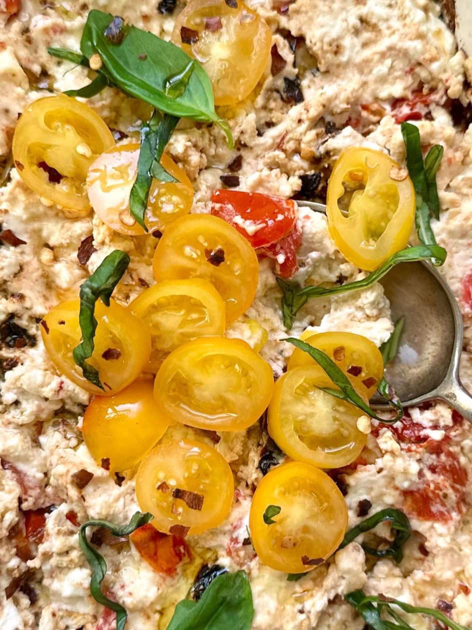 Close up image of hot baked feta cheese dip, topped with fresh tomatoes and shredded basil leaves.