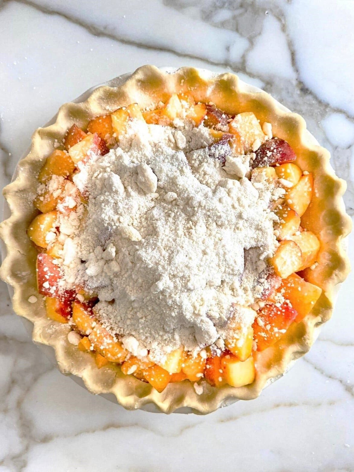 A pastry lined baking dish with diced peaches, topped with crumble topping.
