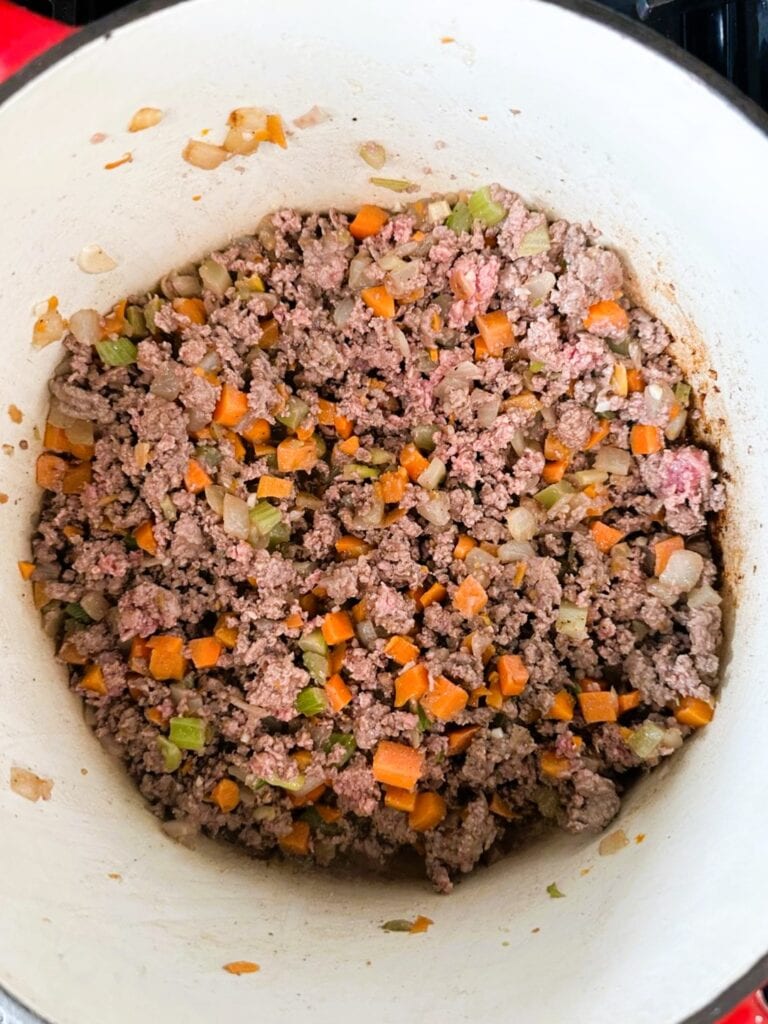 A Dutch oven filled with browned ground meat and diced cooked vegetables.
