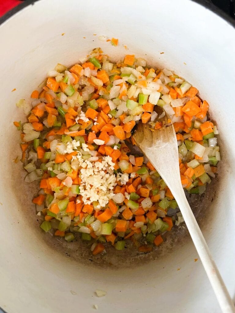 A Dutch oven filled with browned ground meat with added diced onion, celery, carrot and crushed garlic.
