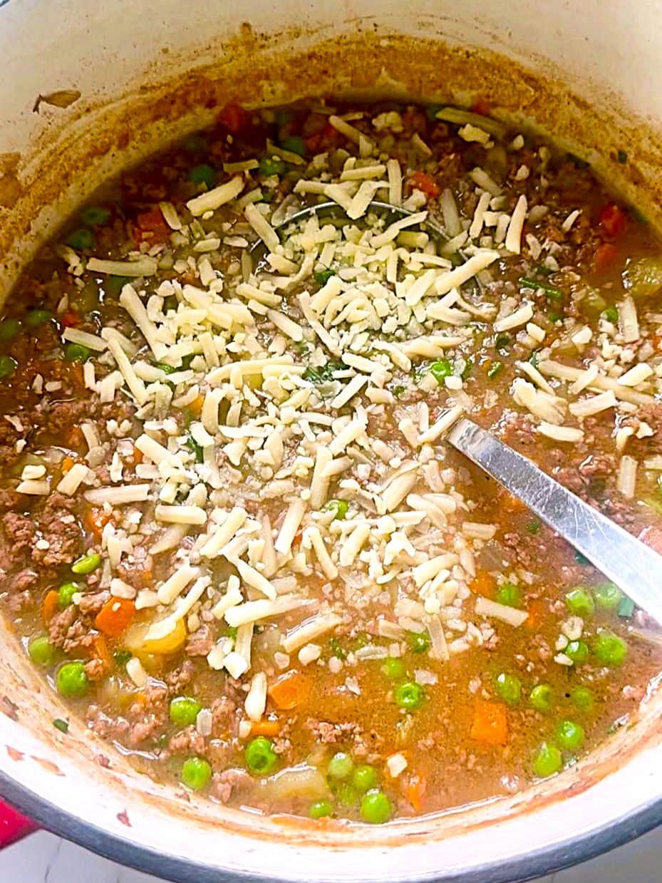 A Dutch oven of cooked shepherd's pie soup with grated/shredded cheese added.