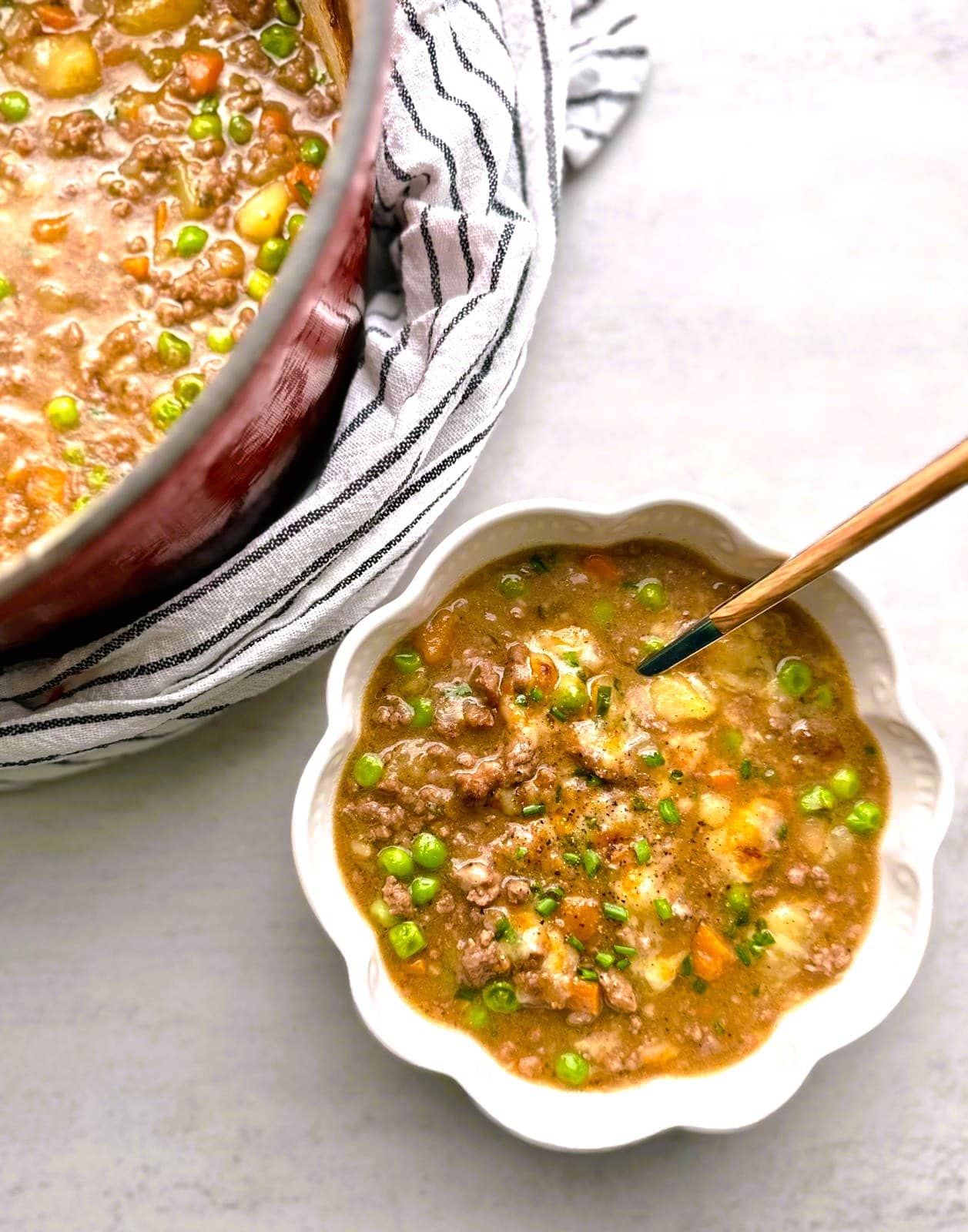 A bowl of hearty shepherd's pie soup garnished with freshly chopped chives, with a pot of soup set alongside.