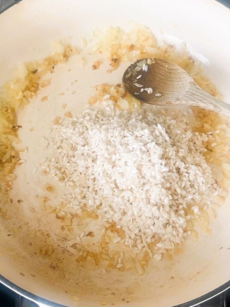 A large skillet with sauteed onions and garlic and added risotto rice.