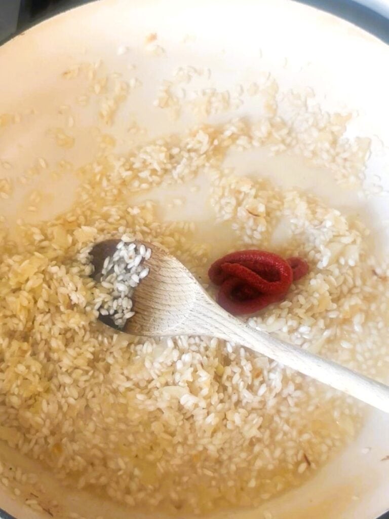 A large skillet of sauteed onion, garlic and rice with added tomato puree.