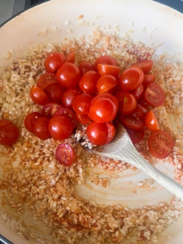 A large skillet with sauteed onion, garlic rice, with added tomato paste and fresh cherry tomato halves.