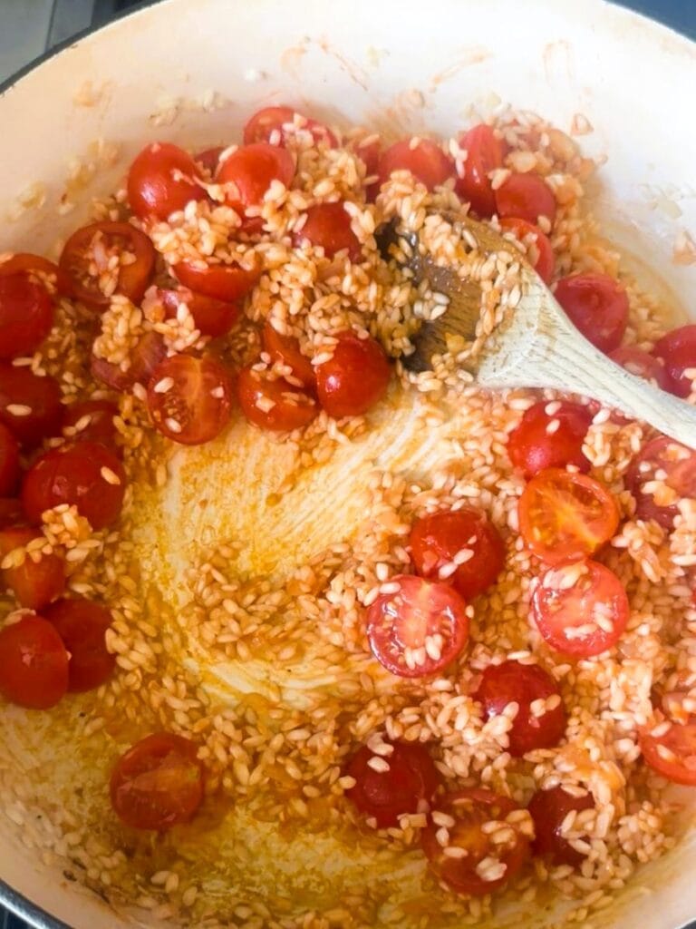 A large skillet with sauteed onion, garlic rice, with added tomato paste and fresh cherry tomato halves.