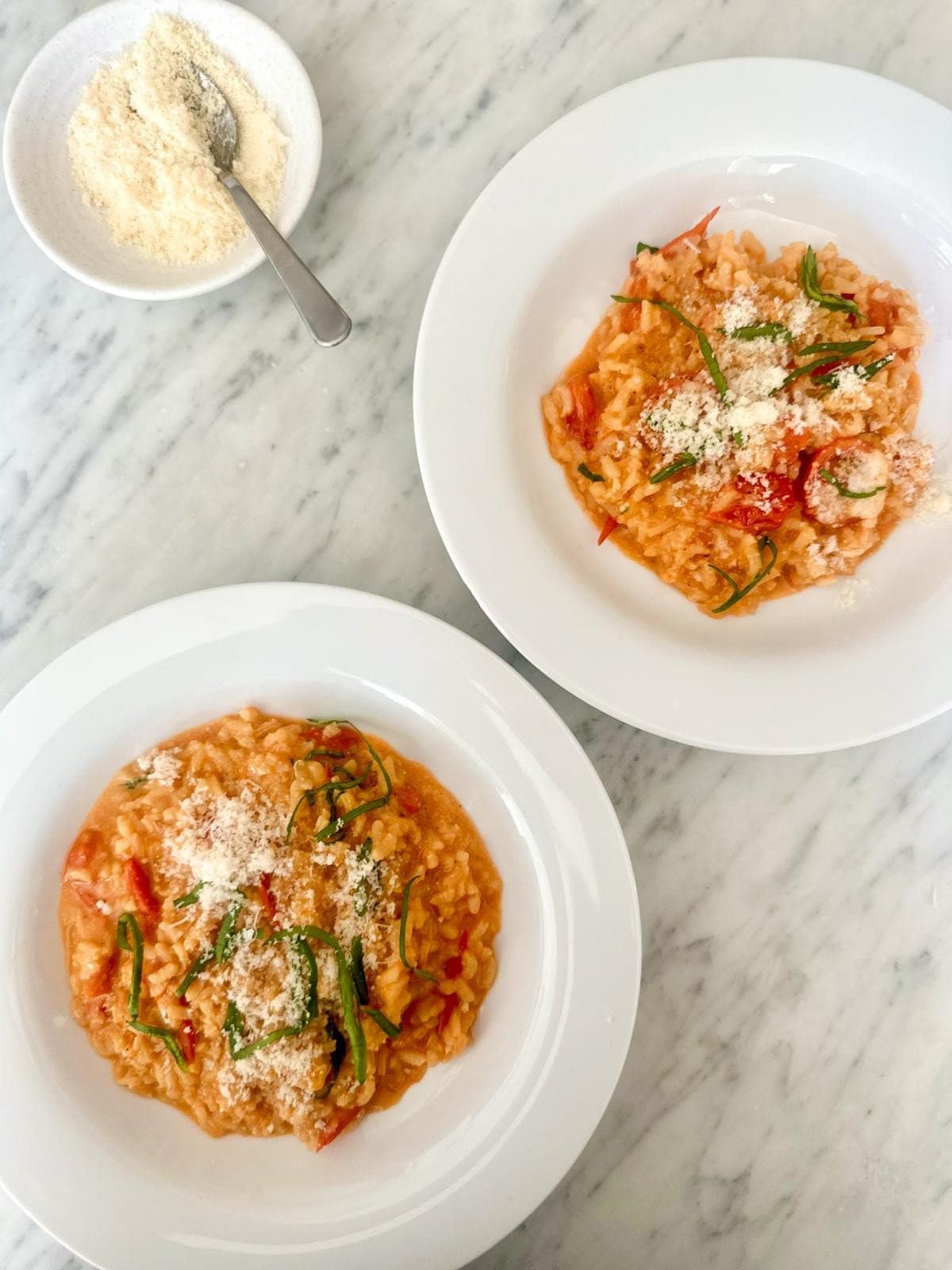 Two bowls of creamy cherry tomato risotto, garnished with fresh basil and parmesan cheese.