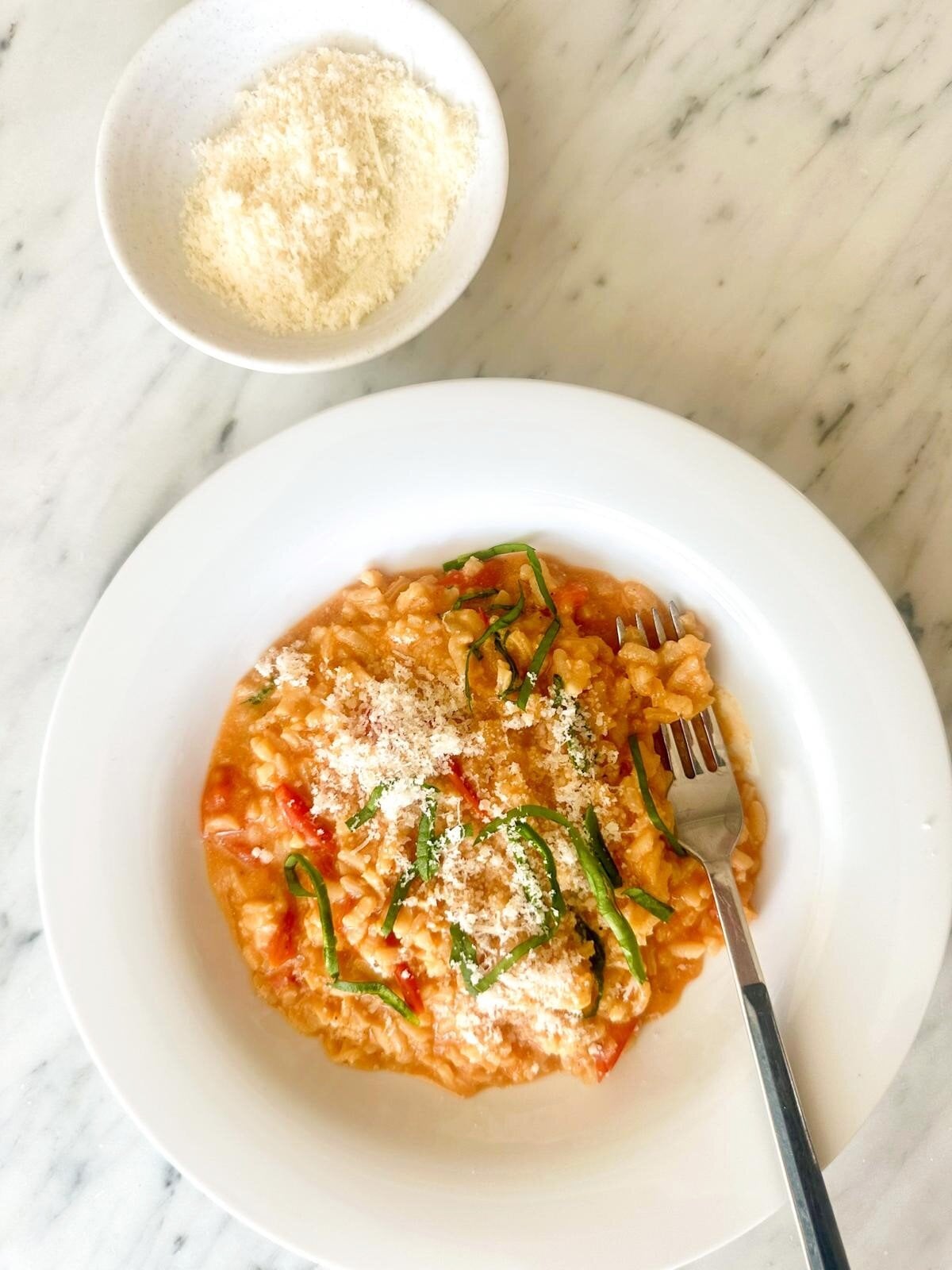 A bowl of creamy cherry tomato risotto, garnished with fresh basil and parmesan cheese.
