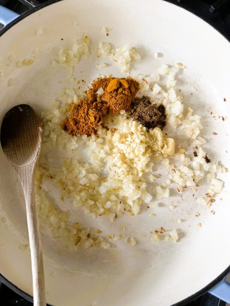 A Dutch oven with sauteed onion with added garlic, ginger and ground spices.