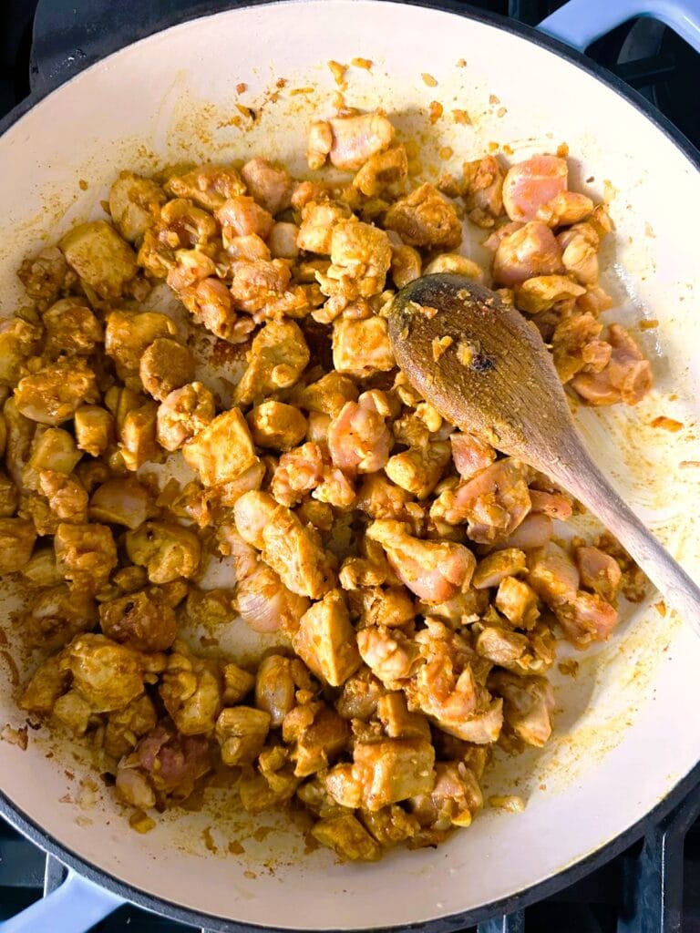 A Dutch oven with chopped onion with added diced chicken.