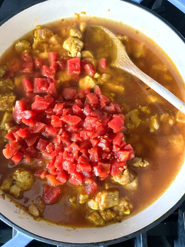 A Dutch oven of cooked chicken in stock with added chopped tomatoes.