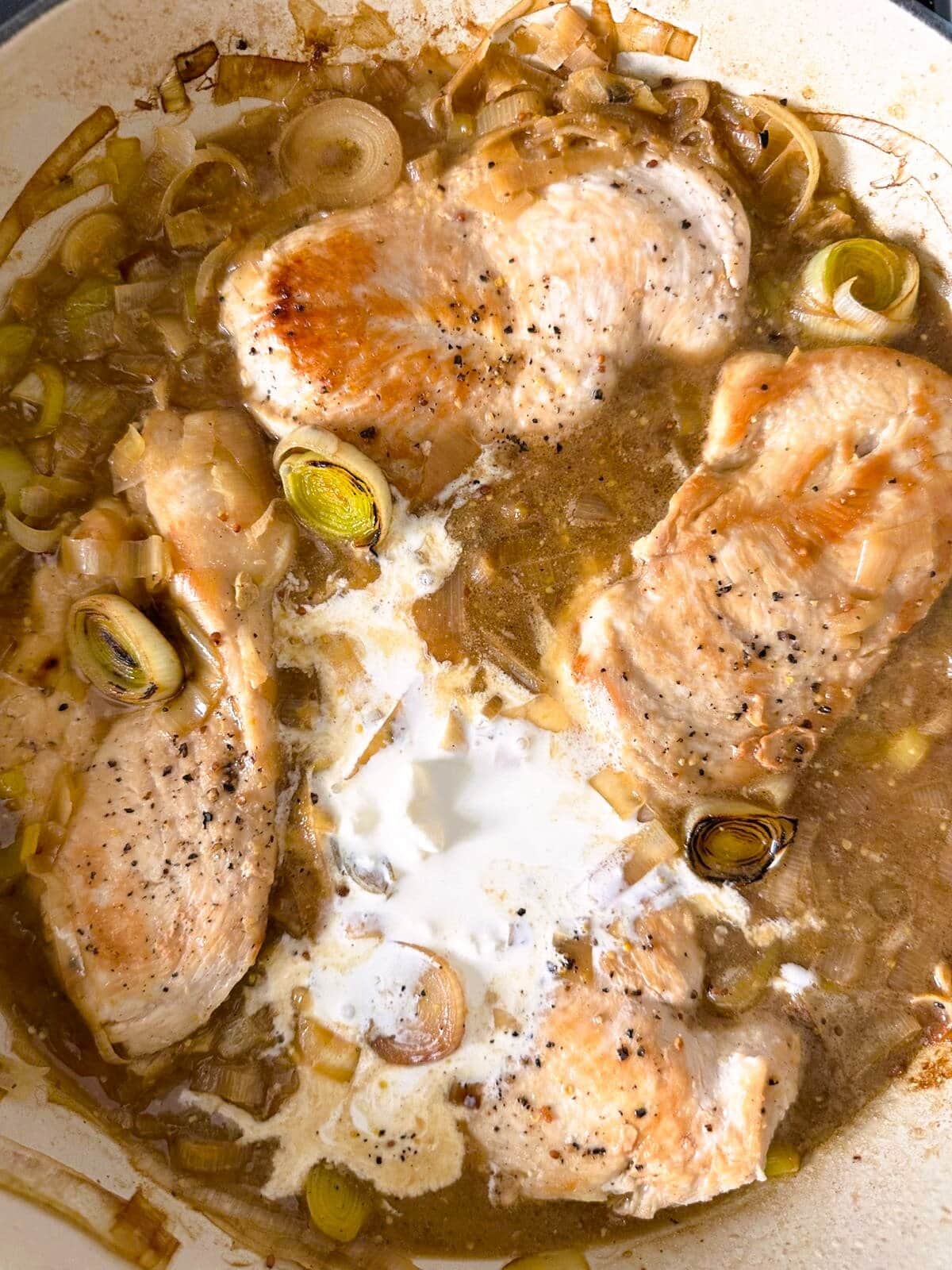 A large skillet of cooked chicken breasts in a leek and stock based sauce, with heavy cream added.
