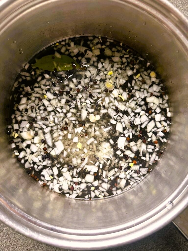 A large saucepan of lentils, chopped onion and garlic with added vegetable stock.