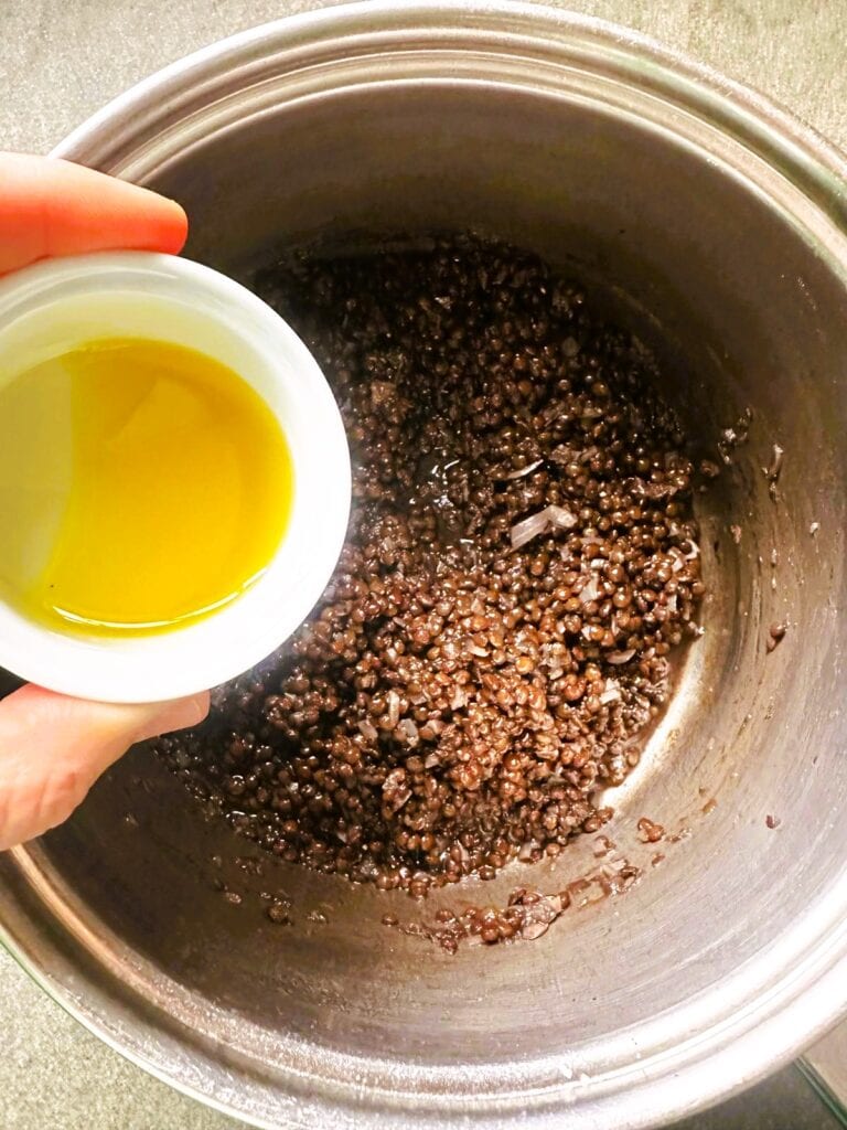 A large saucepan of cooked lentils with olive oil being added.