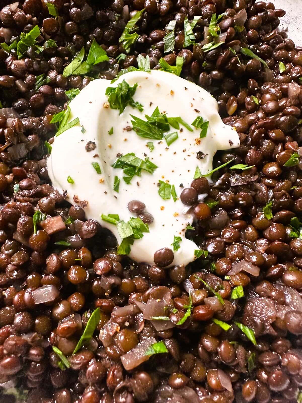 Close up image of black lentils (beluga lentils) topped with a spoon of thick Greek yogurt and a garnish of freshly chopped parsley.