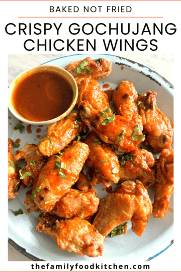 Pinnable image with recipe title and a plate of crispy chicken  wings coated in gochujang glaze with a bowl the dipping sauce set alongside.