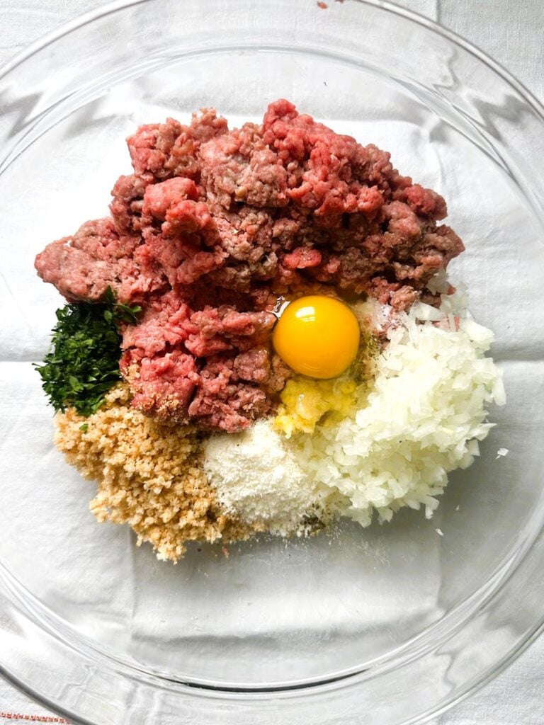 A large mixing bowl of individual ingredients for making gluten-free meatballs.