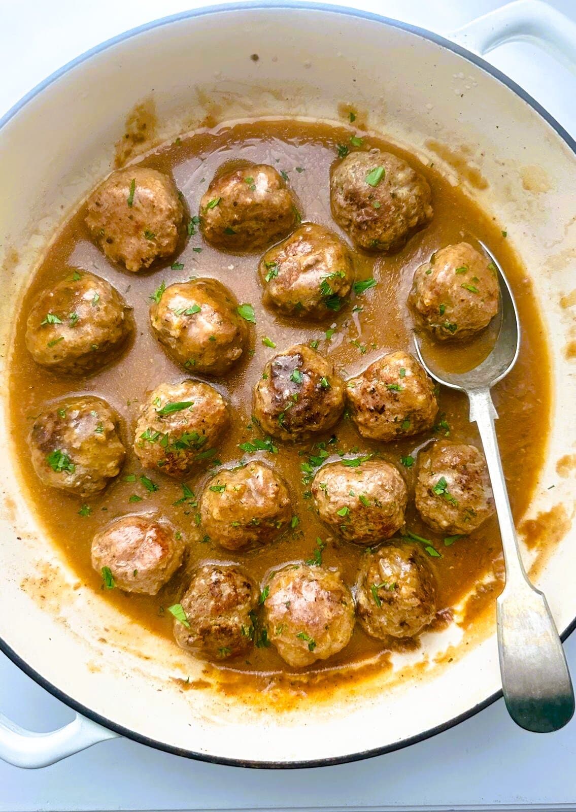 A Dutch oven of gluten-free meatballs in gravy, garnished with fresh parsley.