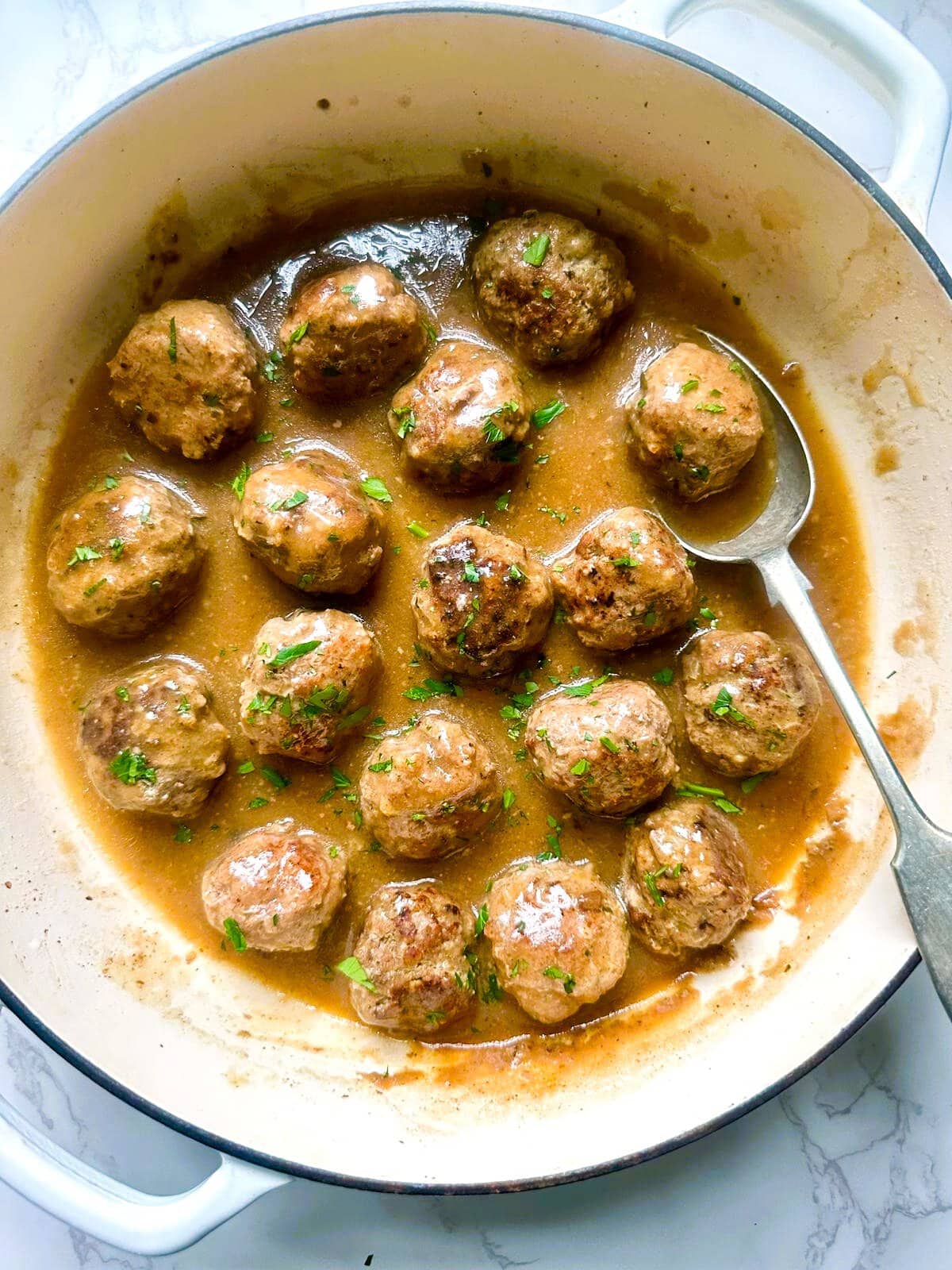 A Dutch oven with gluten-free meatballs in gravy, garnished with fresh parsley.