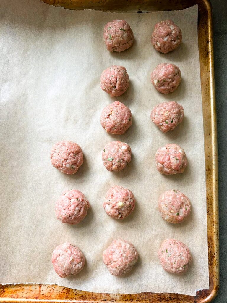 A line baking sheet topped with raw meatballs.