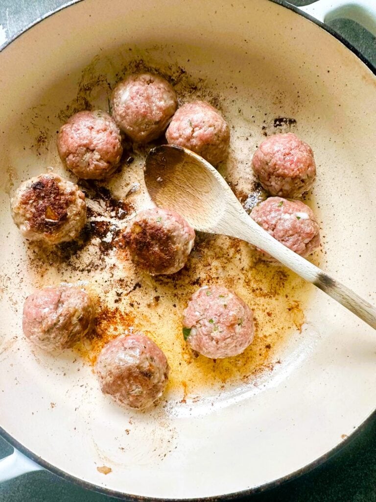 A Dutch oven with gluten-free meatballs being browned in olive oil.