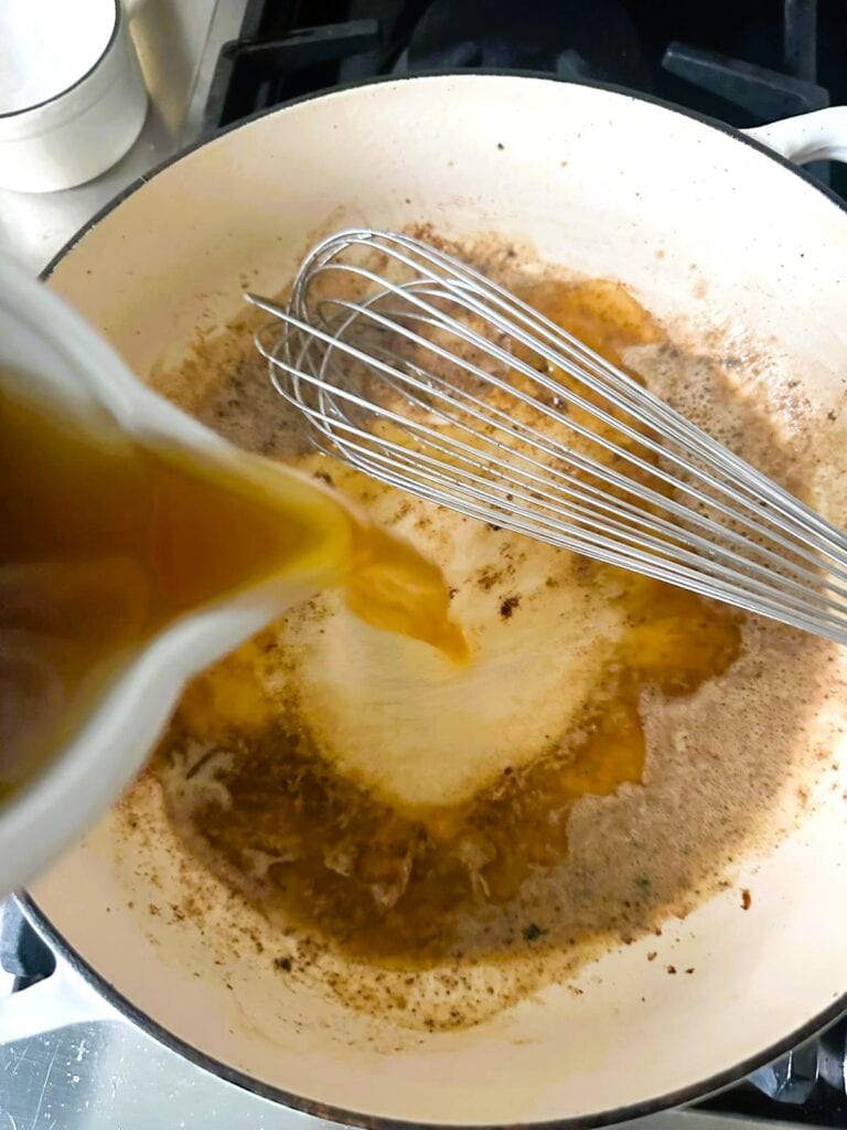 A Dutch oven with pan juices with beef broth being added.