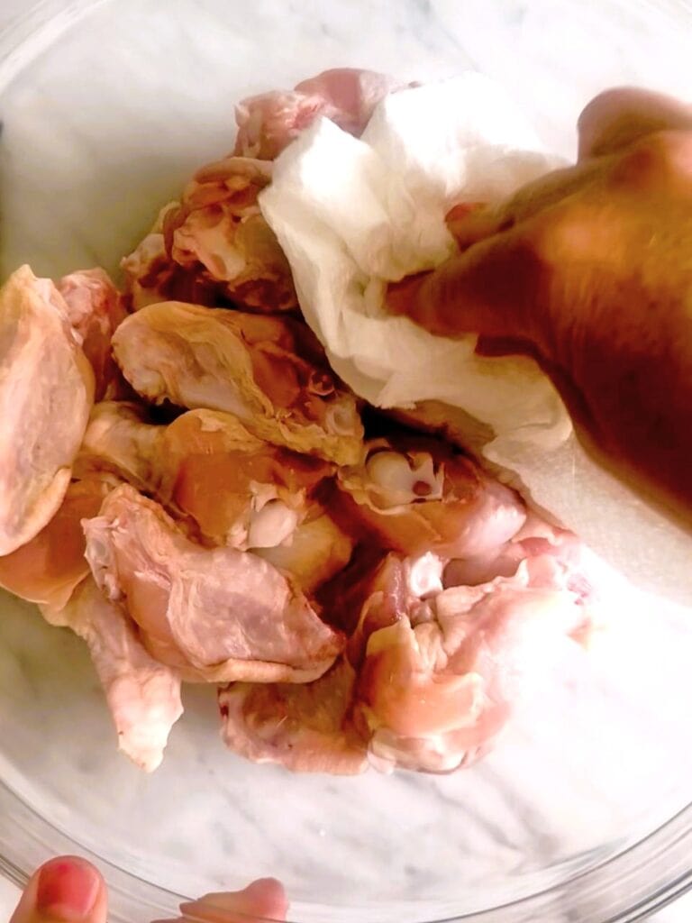 A bowl of raw chicken wings being patted dry with kitchen towel.