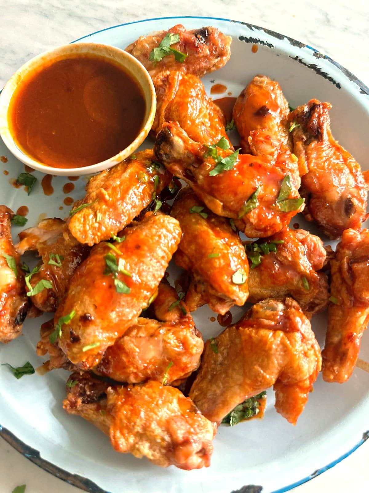 A plate of crispy chicken  wings coated in gochujang glaze with a bowl the dipping sauce set alongside.