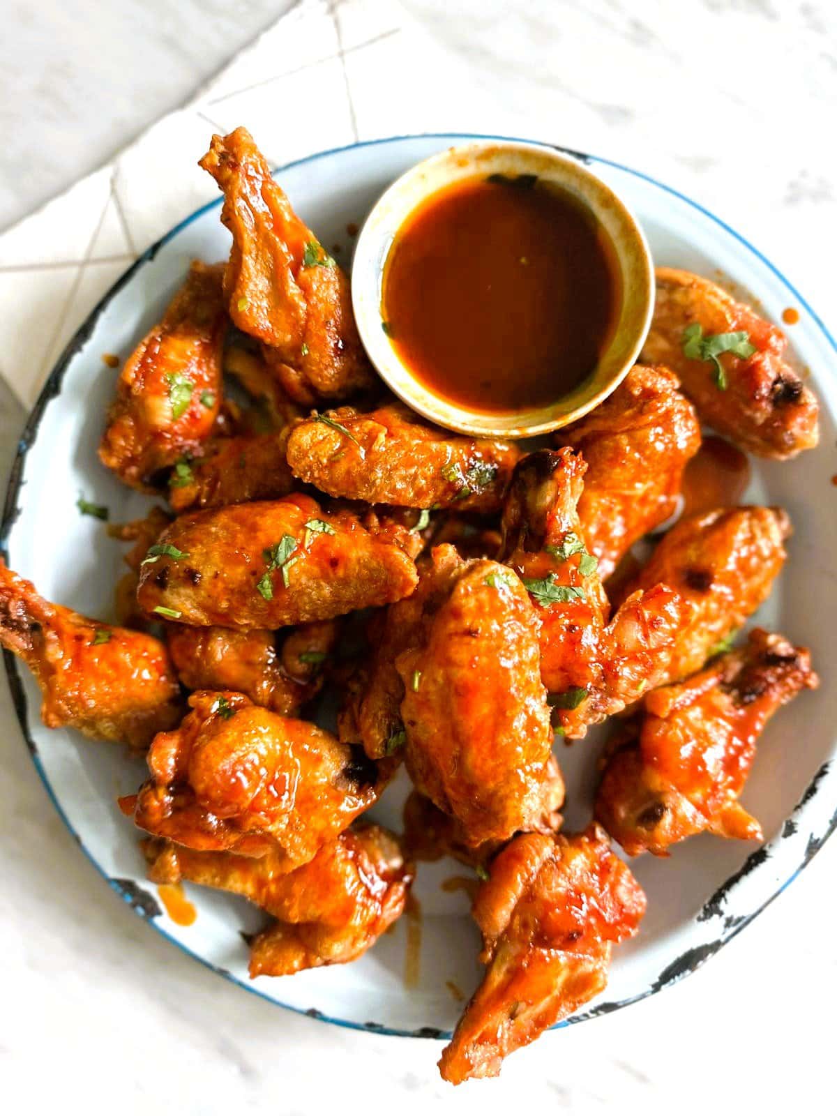 A plate of crispy chicken  wings coated in gochujang glaze with a bowl the dipping sauce set alongside.