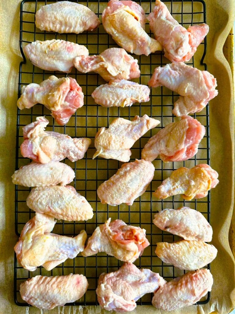 Raw chicken wings set on a wire rack over a baking tray lined with baking parchment.
