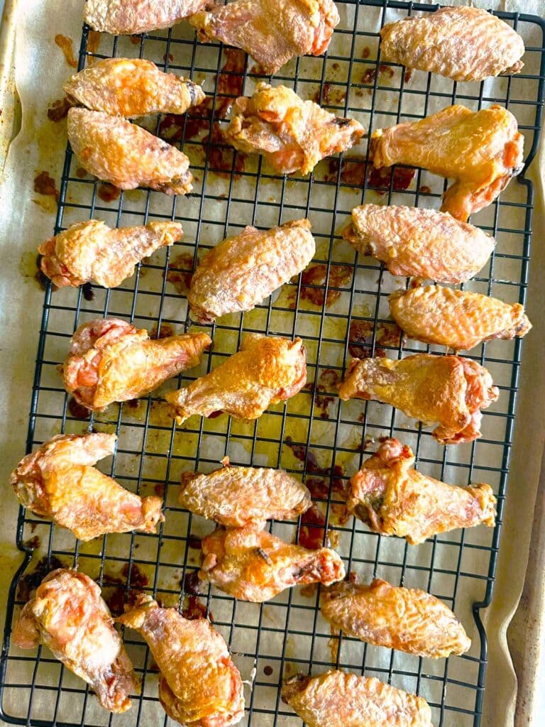Crispy chicken wings set on a wire rack over a baking tray lined with baking parchment.