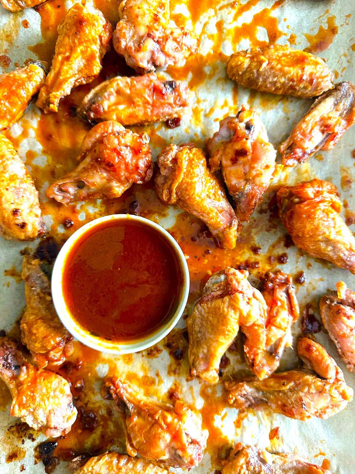 Close up image of crispy chicken  wings coated in gochujang glaze with a bowl the dipping sauce set alongside.