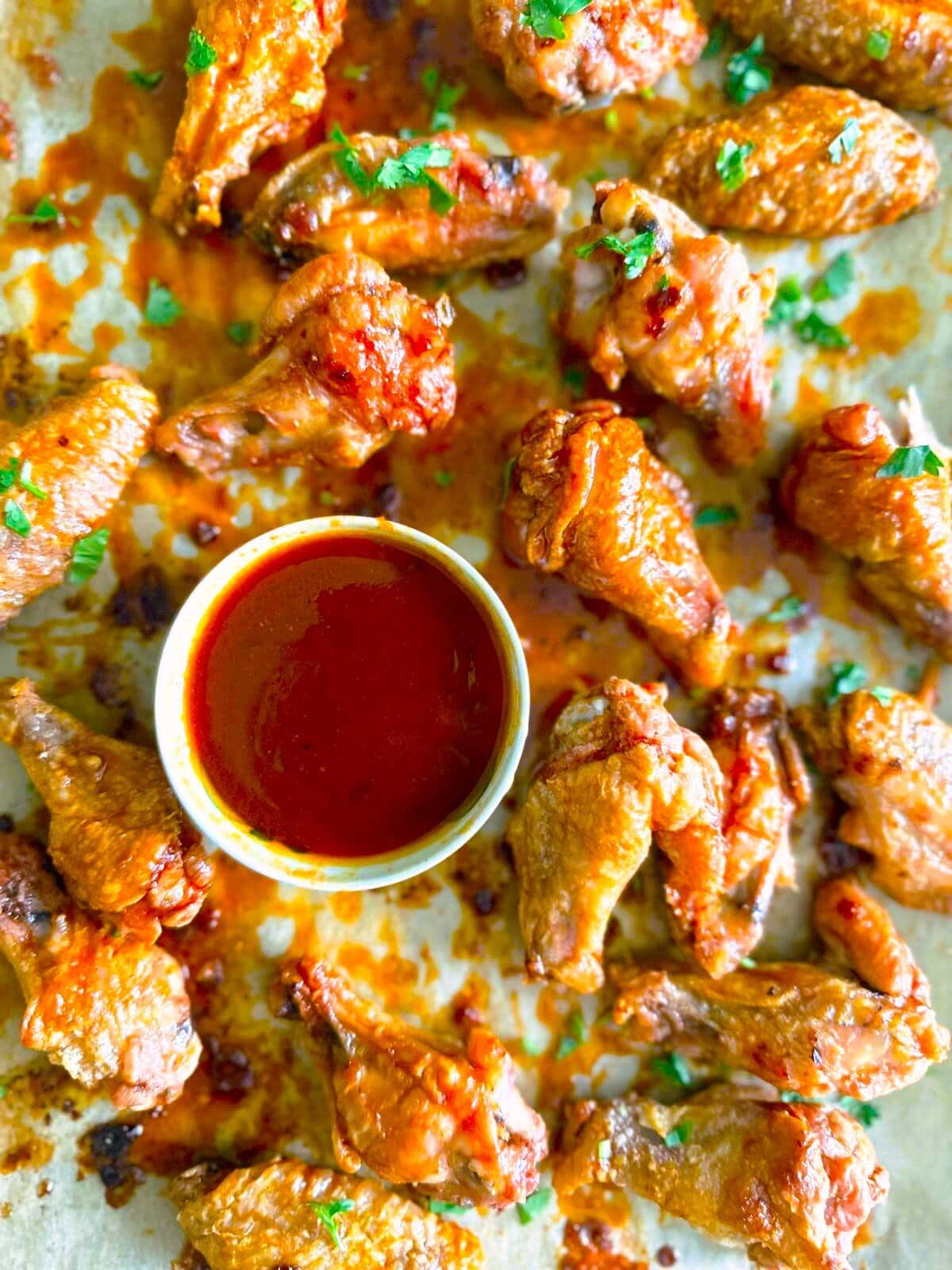 Close up image of crispy chicken  wings coated in gochujang glaze with a bowl the dipping sauce set alongside.