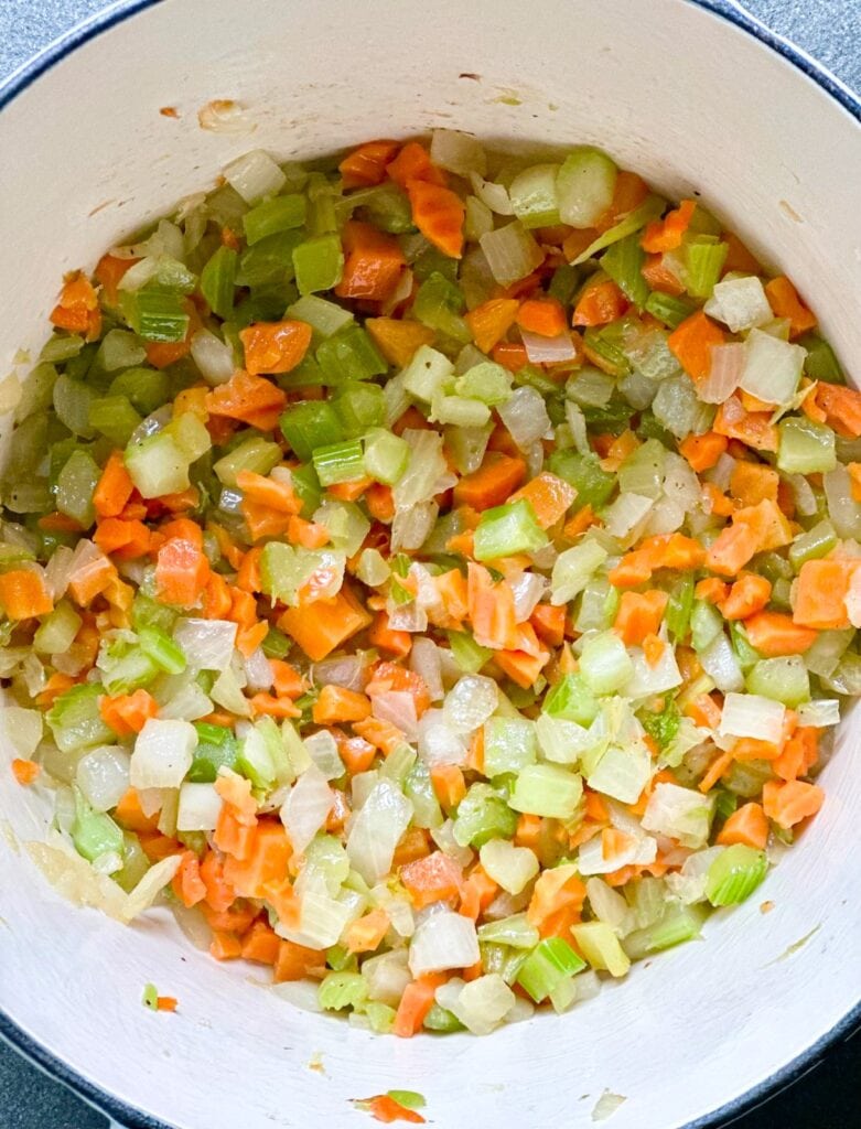 A Dutch oven with diced and sauteed onion, celery and carrot.