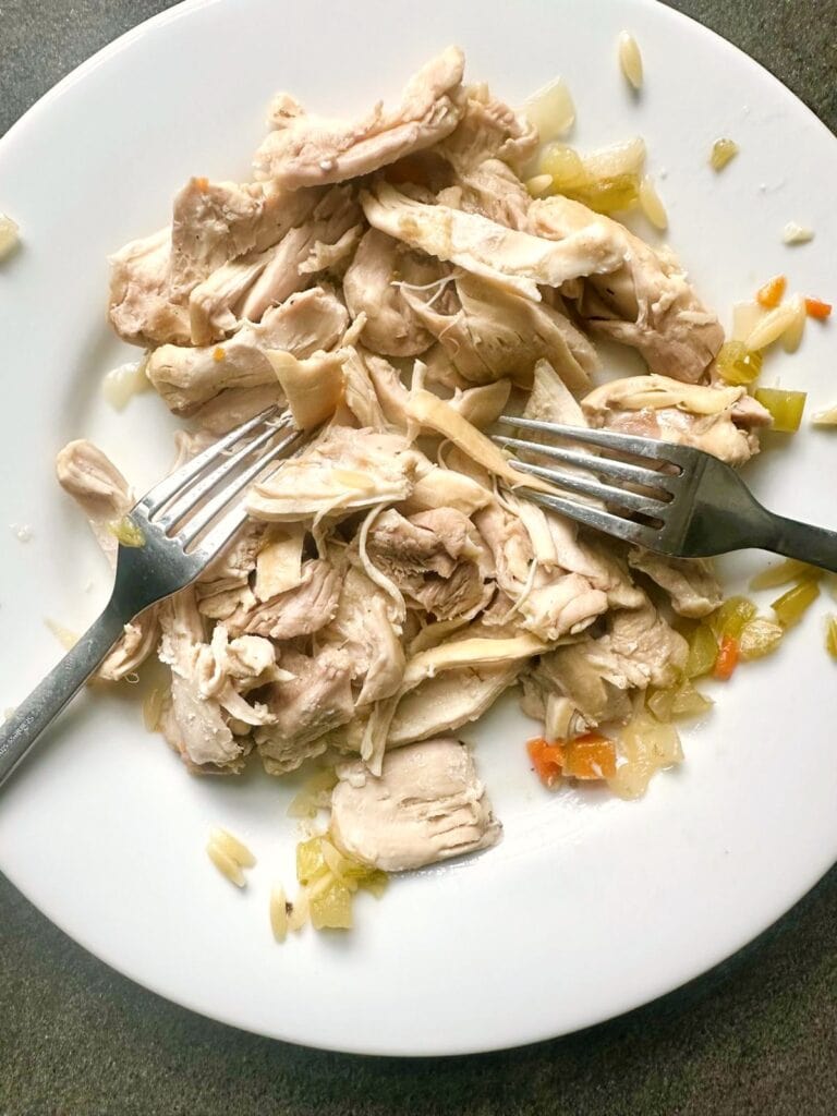 Cooked chicken thighs being shredded on a plat with two forks.