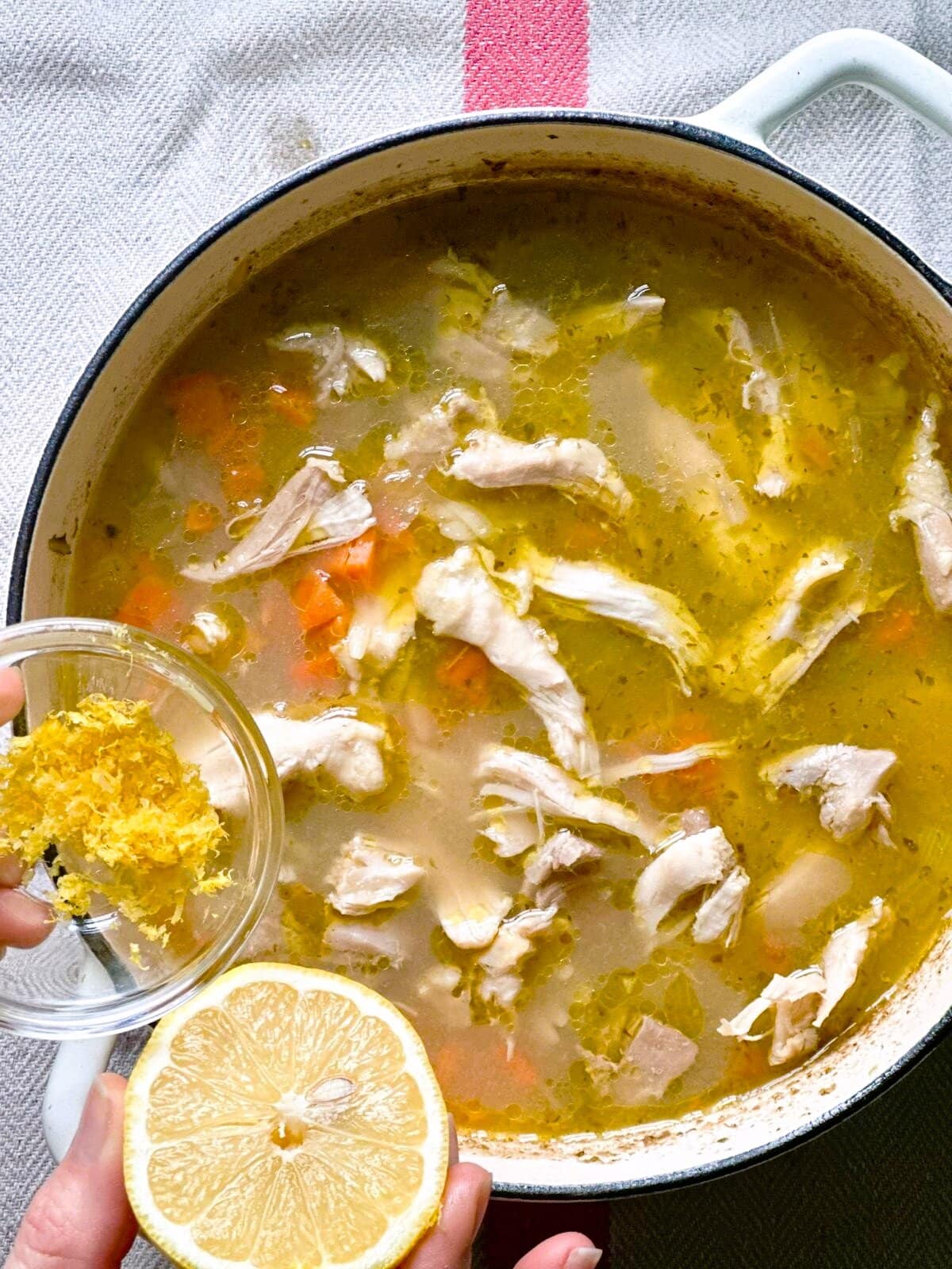 A Dutch oven of lemon chicken soup with lemon zest being added.