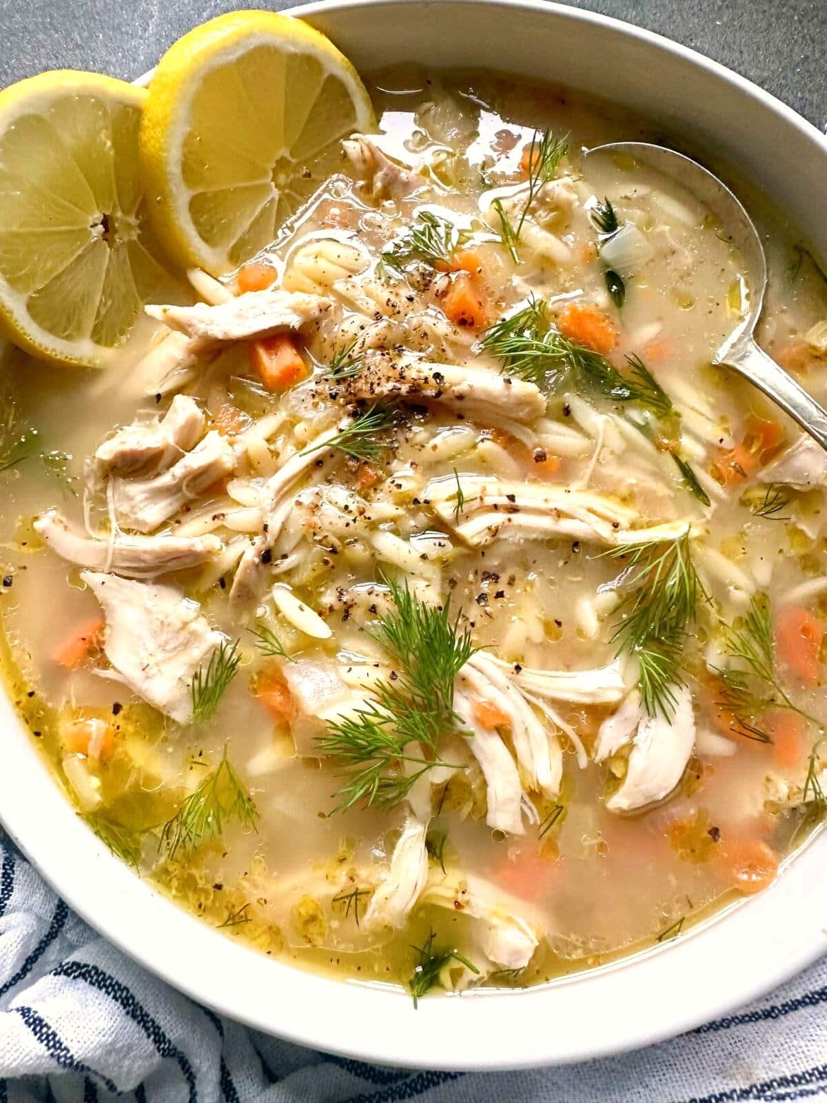 A bowl of lemon chicken orzo soup, garnished with fresh dill fronds and fresh lemon slices.