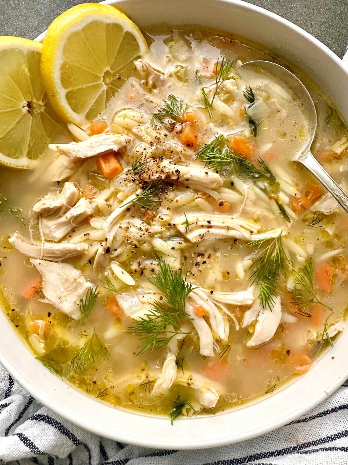 A bowl of lemon chicken orzo soup, garnished with fresh dill fronds and fresh lemon slices.