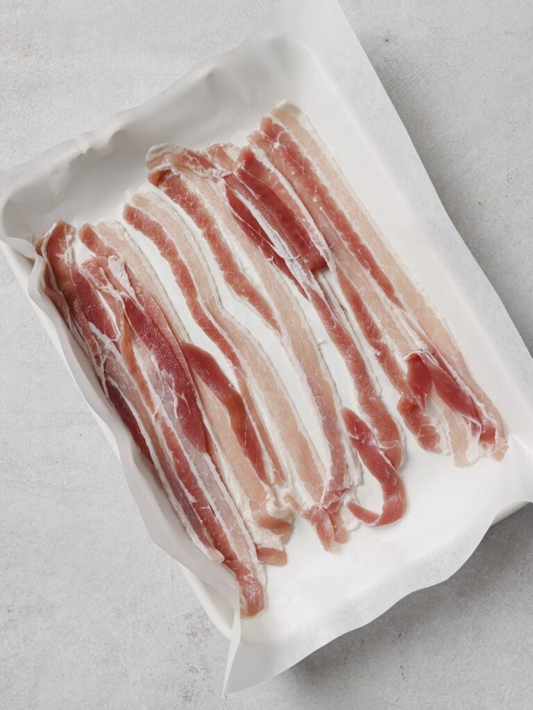A lined baking sheet topped with slices of raw bacon.