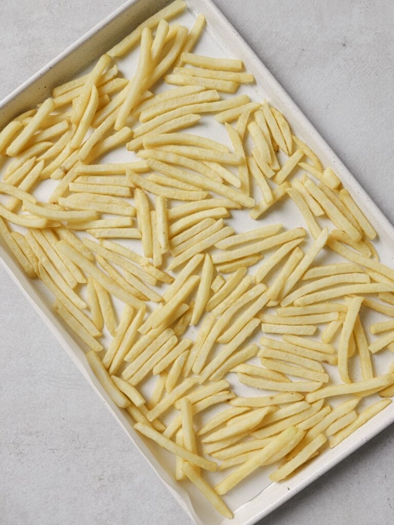 A lined baking sheet topped with a single layer of frozen French fries.
