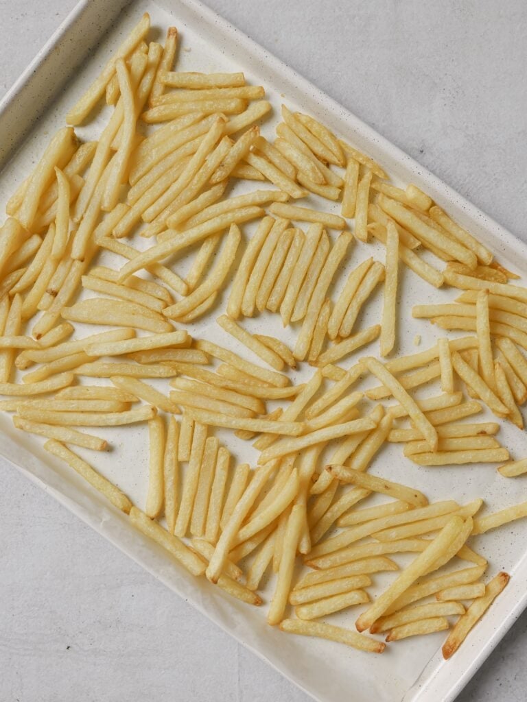 A lined baking sheet topped with part cooked French fries.