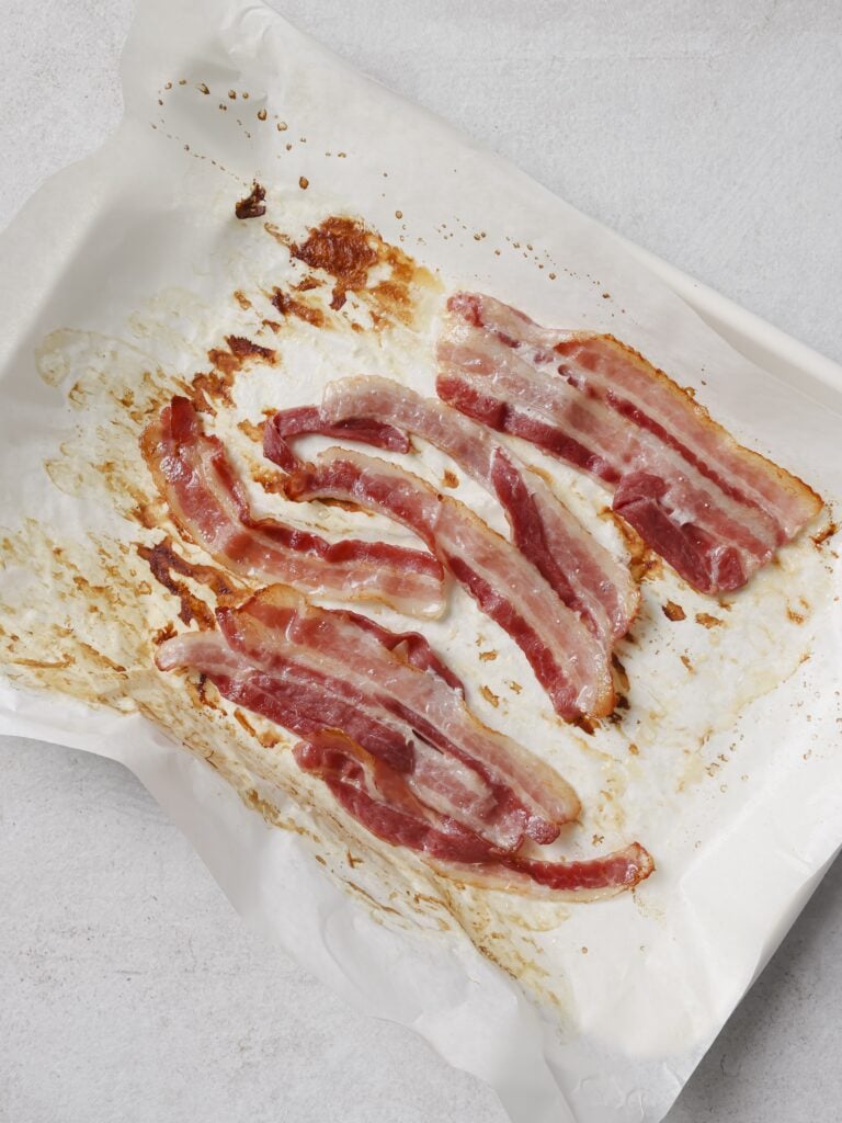 A lined baking sheet topped with cooked bacon strips.