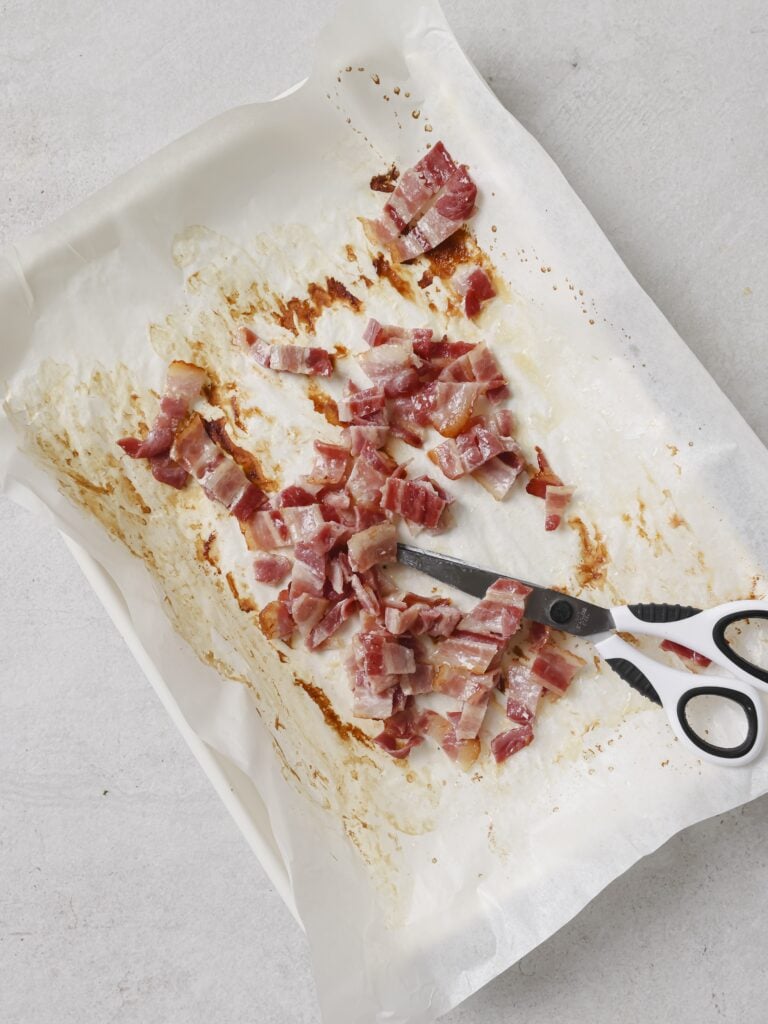 A lined baking sheet with a pair of scissors and cut up bacon pieces.