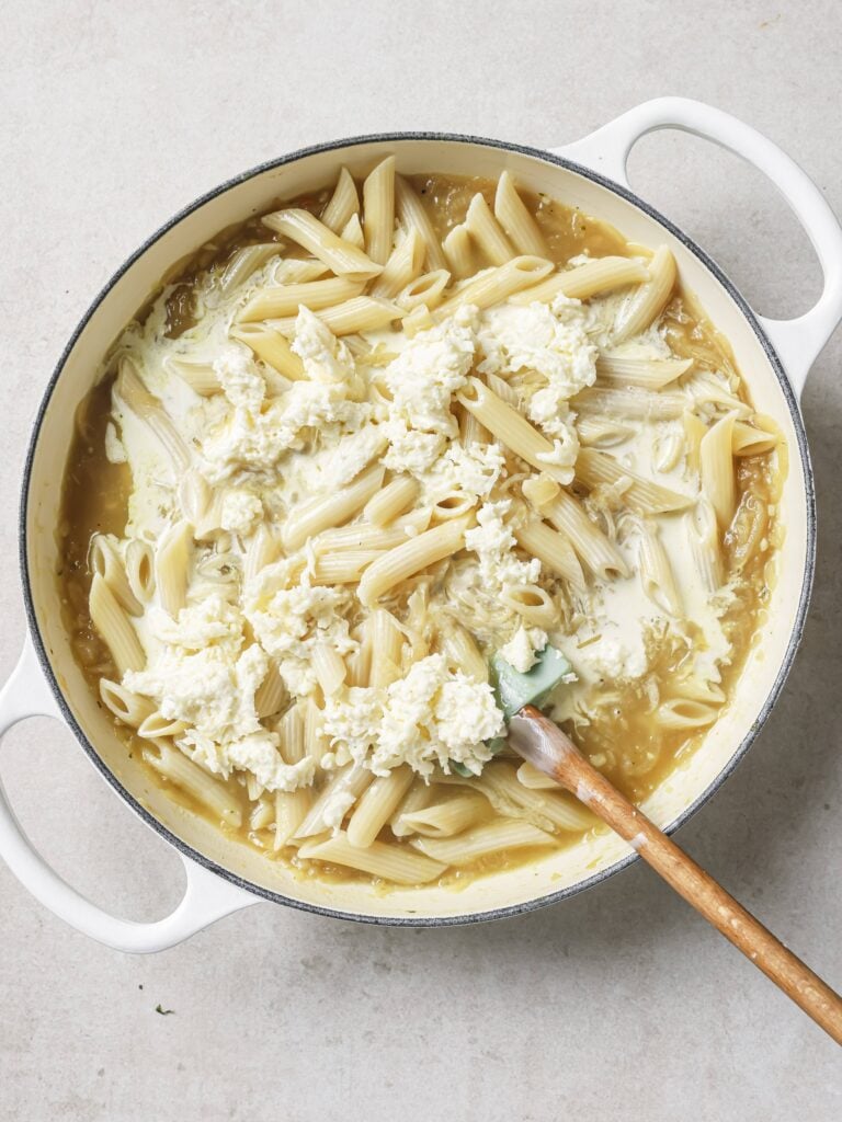 A large skillet of French onion soup pasta with added shredded cheese and cream.