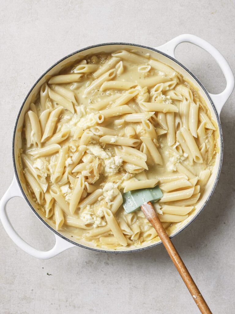A large skillet of French onion soup pasta with more added cheese.