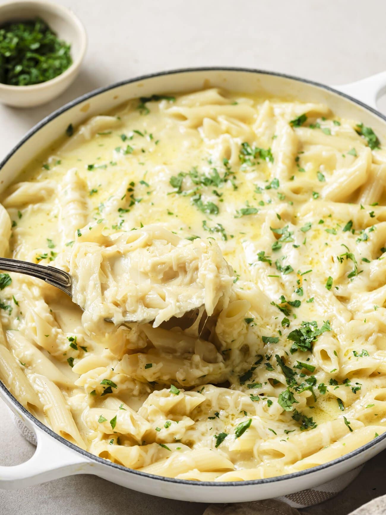 A large skillet of cheesy French onion soup pasta garnished with freshly chopped herbs.